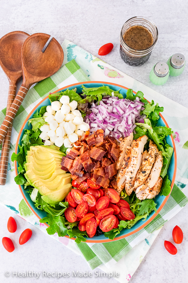 Overhead shot of chicken strips, onion, bacon, tomato, avocado and mozzarella pearls in a bowl on a bed of spring mix.