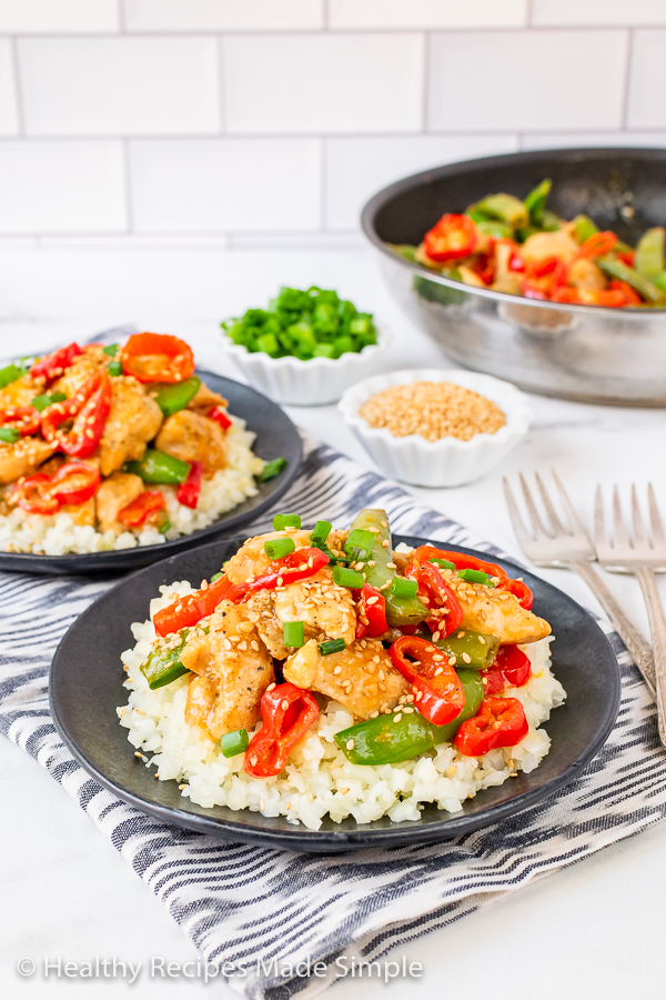 Orange Sesame Chicken on a bed of cauliflower rice served on a black plate.