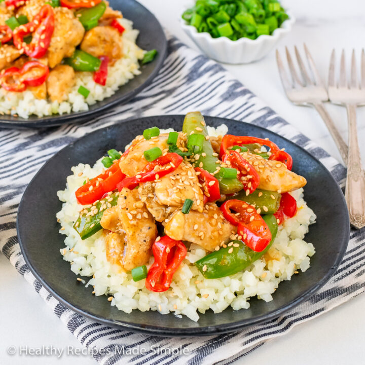 Orange Sesame Chicken on a bed of cauliflower rice served on a black plate.