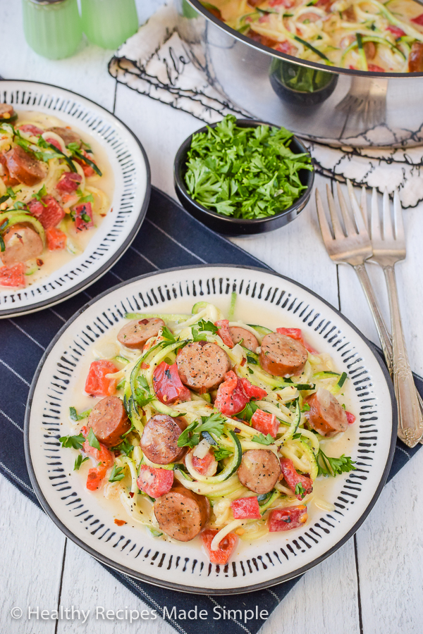 A white plate with zucchini alfredo and chicken sausage on it.