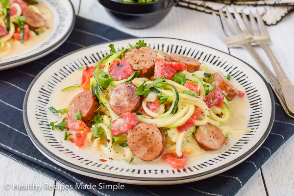 A white plate with chicken sausages and zucchini alfredo noodles on it.