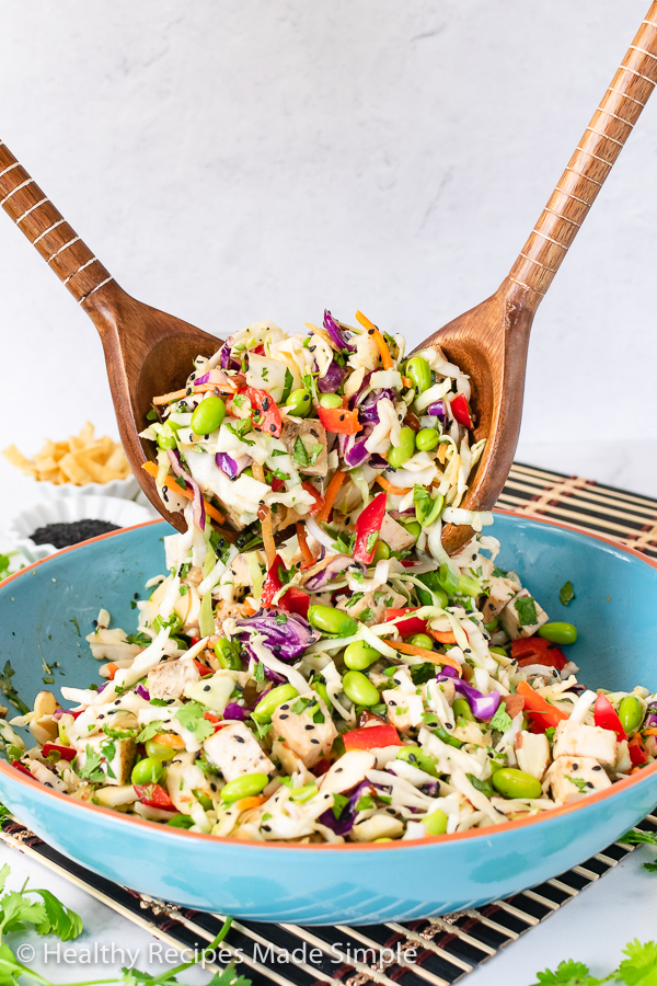 2 wooden serving spoons tossing together ingredients of a salad.