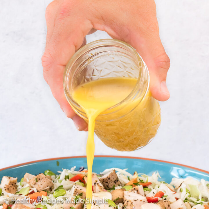 An Asian Salad with a mason jar of Orange Ginger Vinaigrette being poured on it.