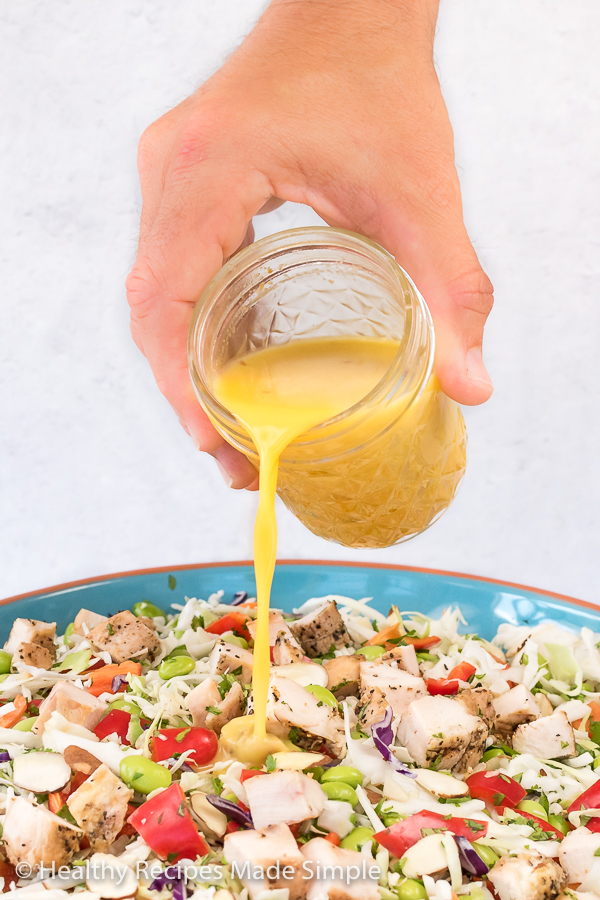 A picture of Orange Ginger Vinaigrette being poured onto an Asian Chopped Chicken Salad.