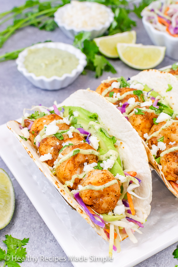 A plate of shrimp tacos topped with cabbage, dressing, and avocado.