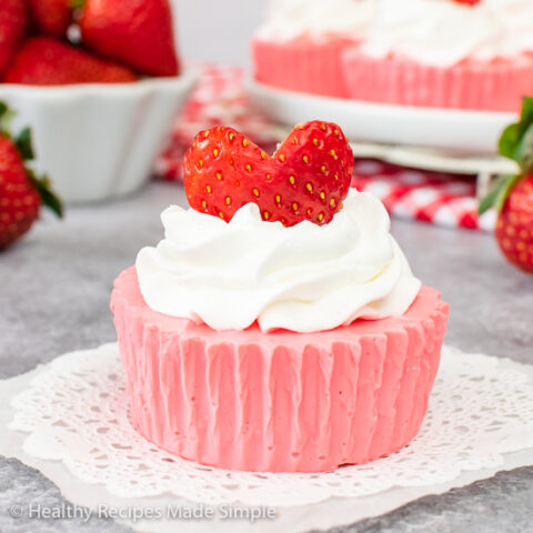 A single piece of pink, creamy jello dessert on a white doily.