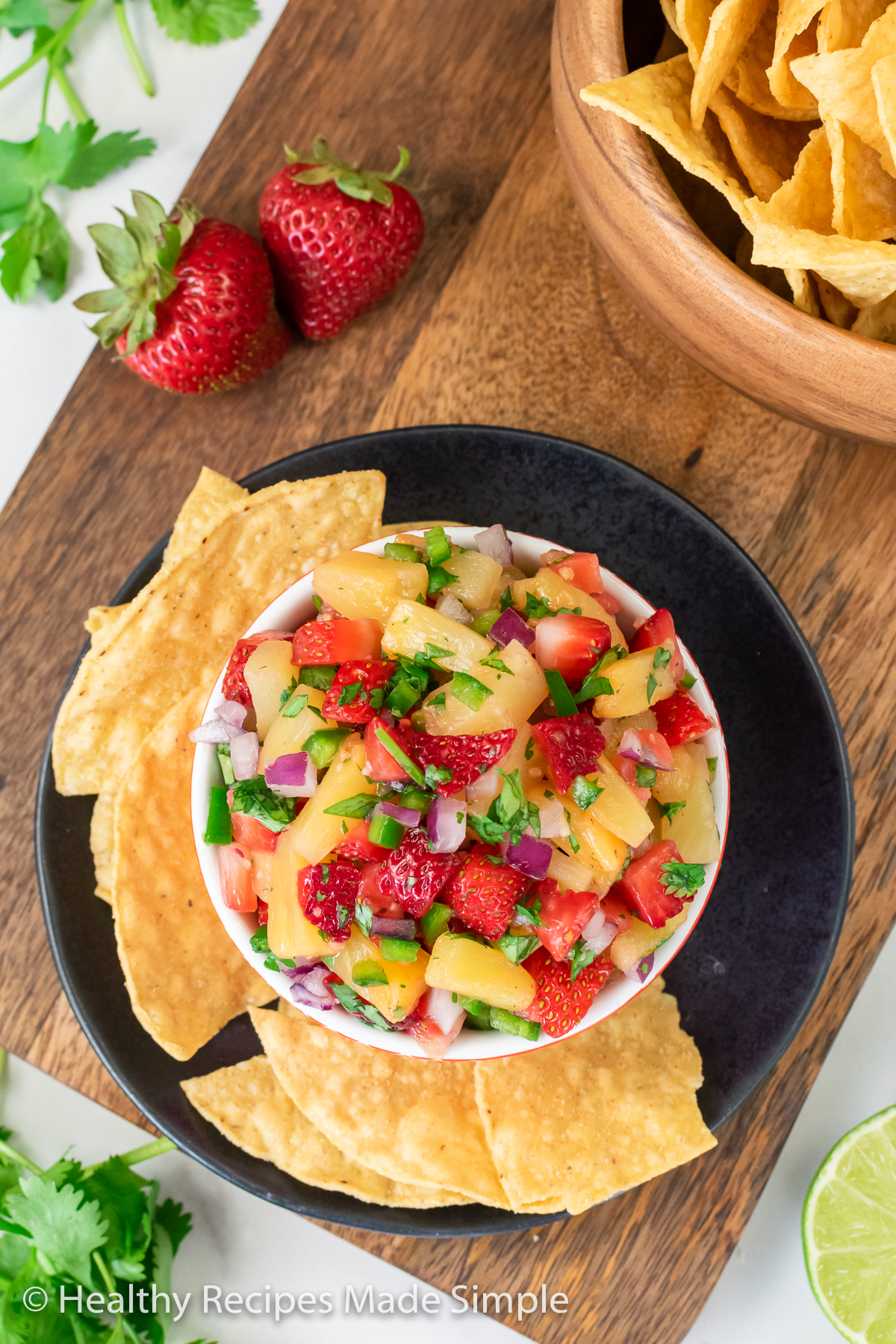 Overhead shot of strawberry pineapple salsa in a bowl on a black plate with chips.