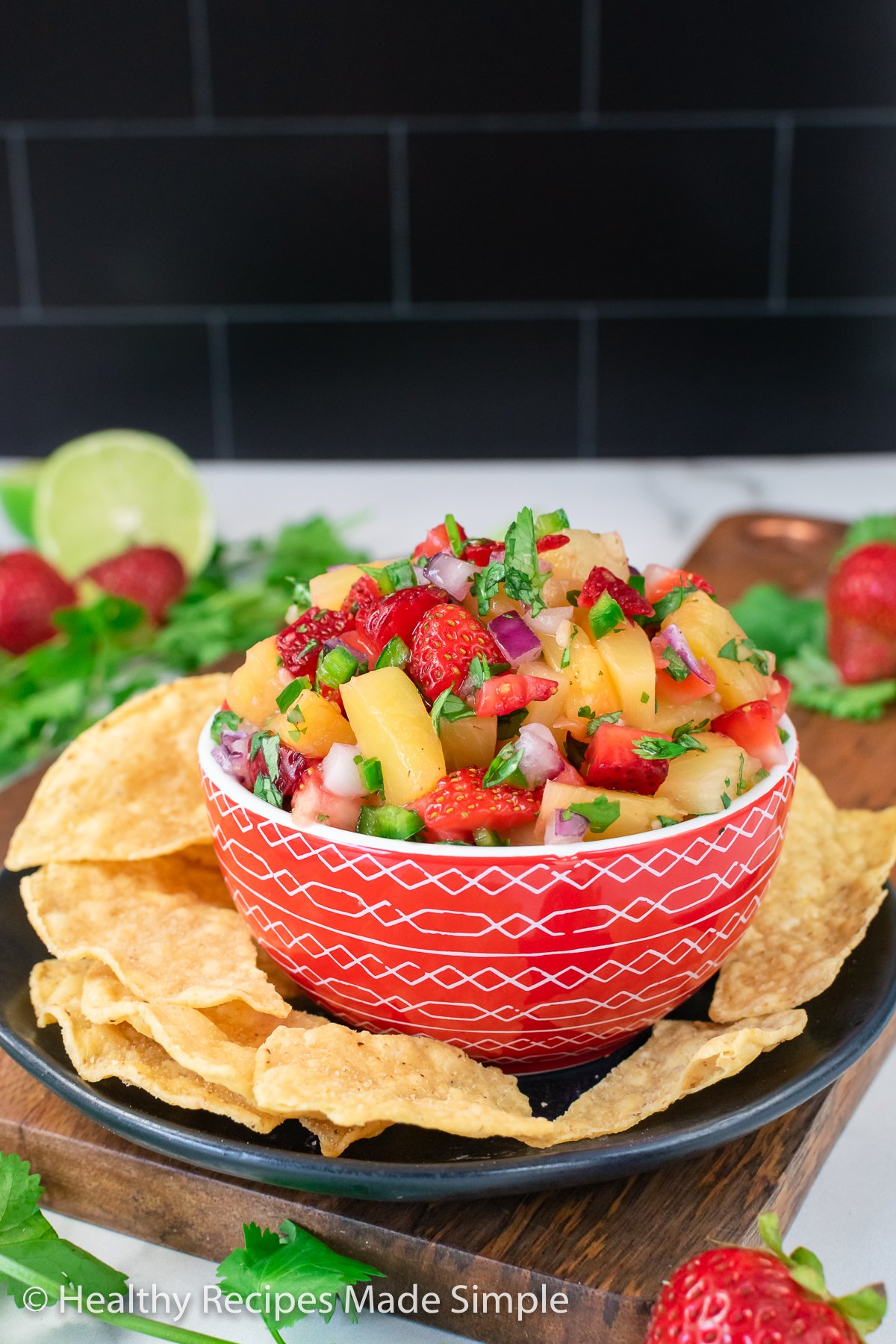 A red bowl full surrounded by chips and filled with Strawberry Pineapple Salsa.