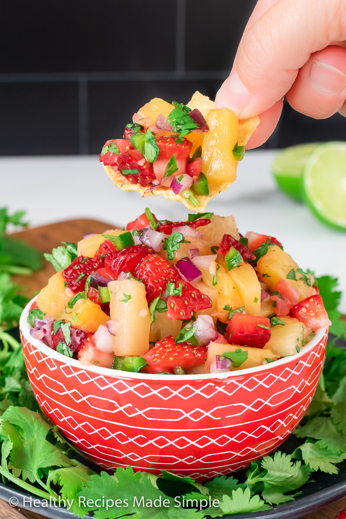 A bowl of Strawberry Pineapple Salsa with a chip being dipped out of it.