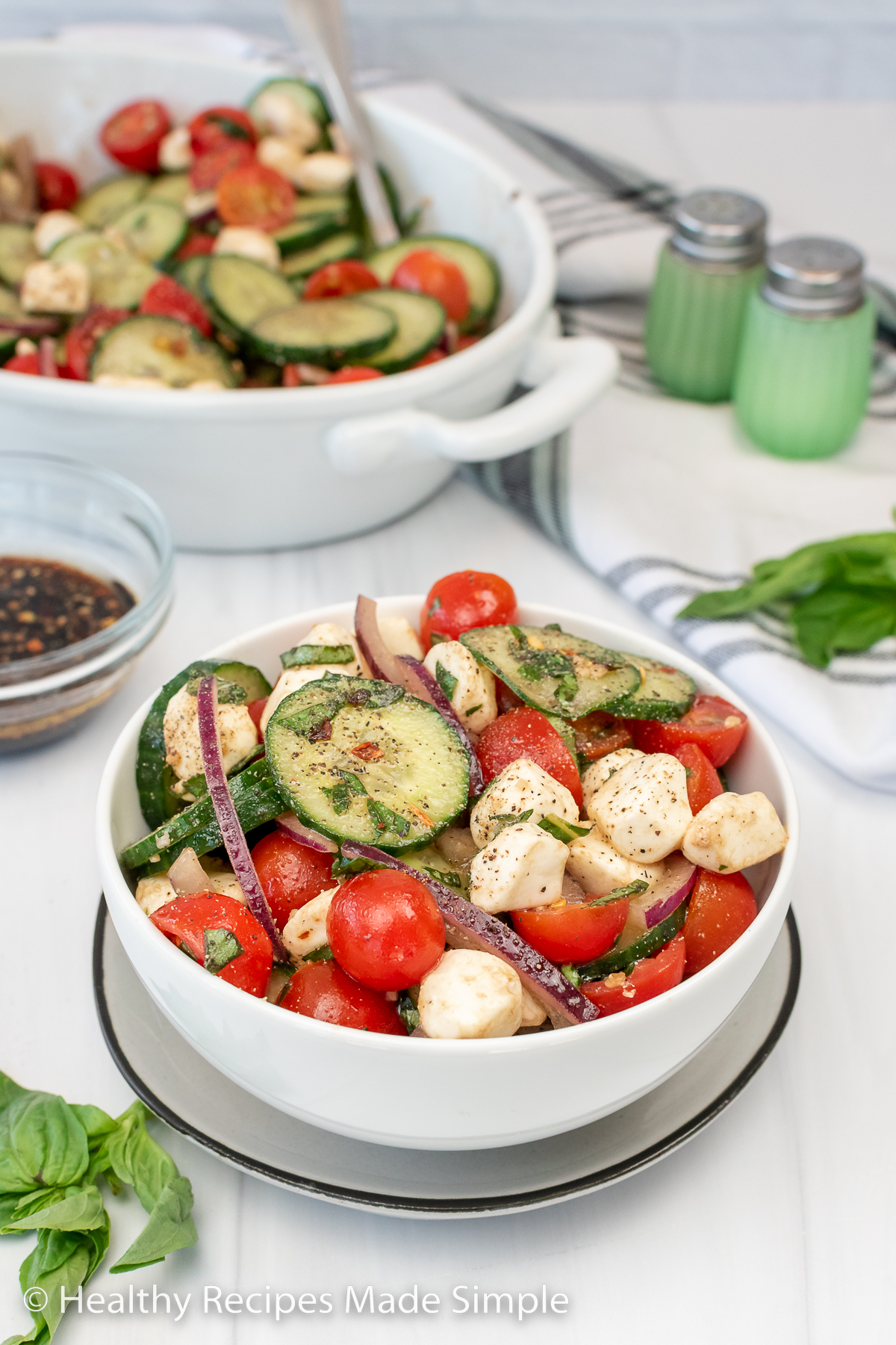 A bowl full of cherry tomatoes, sliced onion, cucumber, and mozzarella balls.