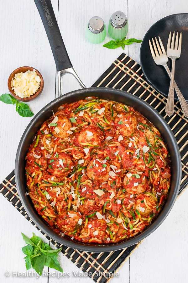 An overhead picture of a pan of zucchini noodles, tomato sauce, and meatballs.