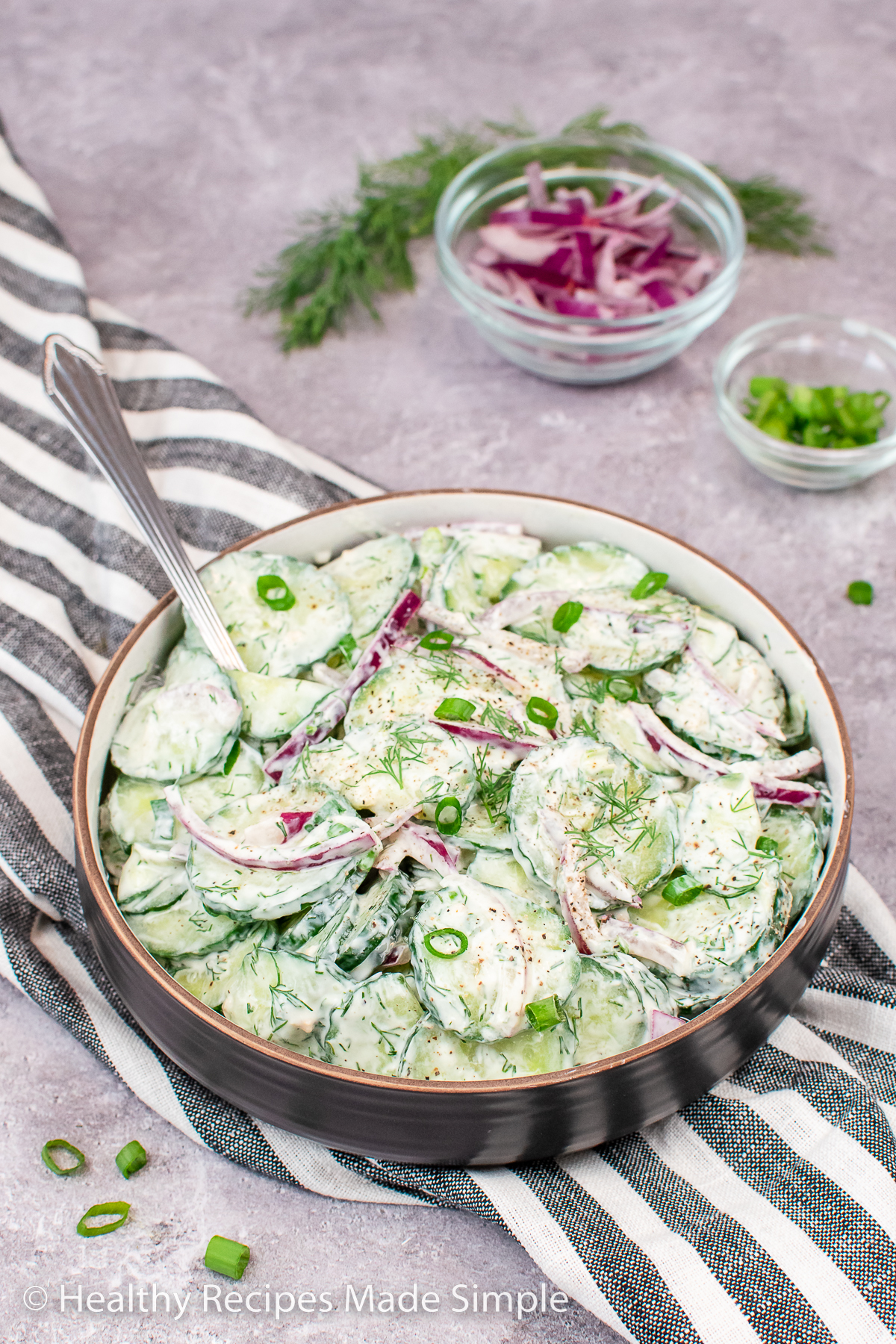 A brown bowl with cucumbers covered in a dill yogurt dressing.