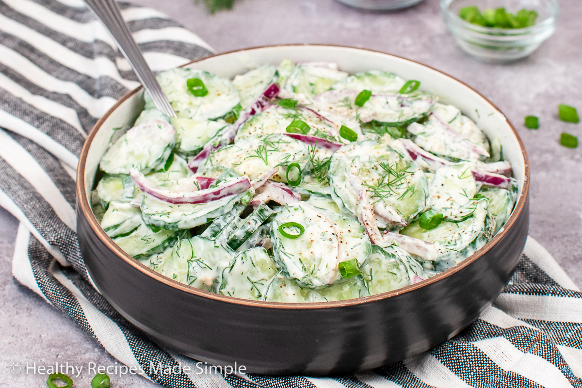 A brown bowl with cucumbers covered in a dill yogurt dressing.