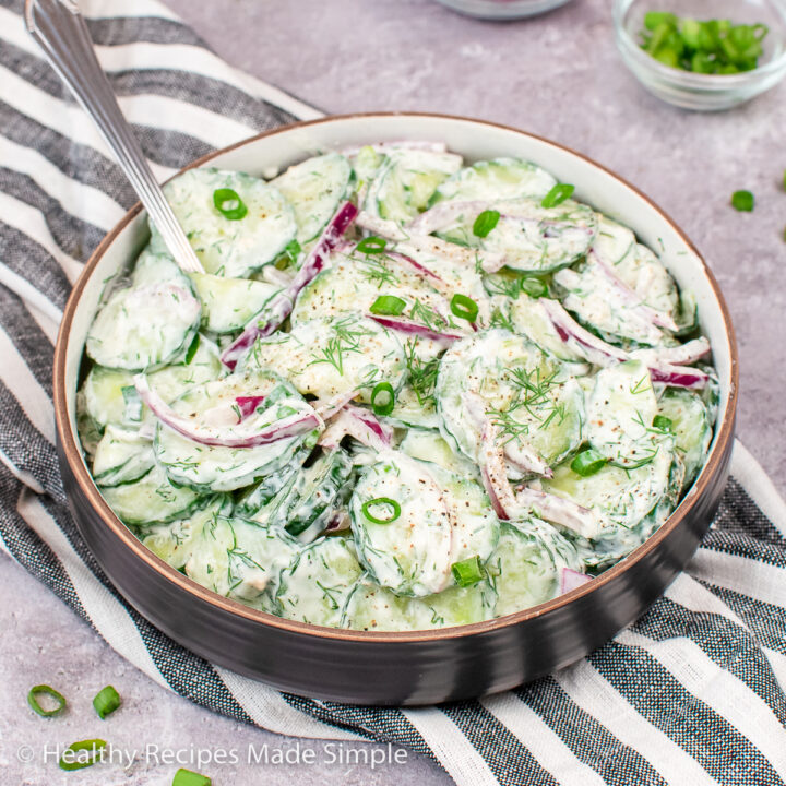 A brown bowl full of cucumber salad with creamy dill dressing.