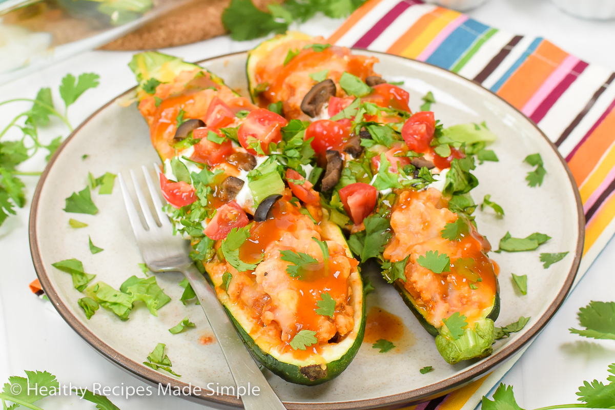 Taco zucchini topped with cheese, cilantro, tomato, and black olives.