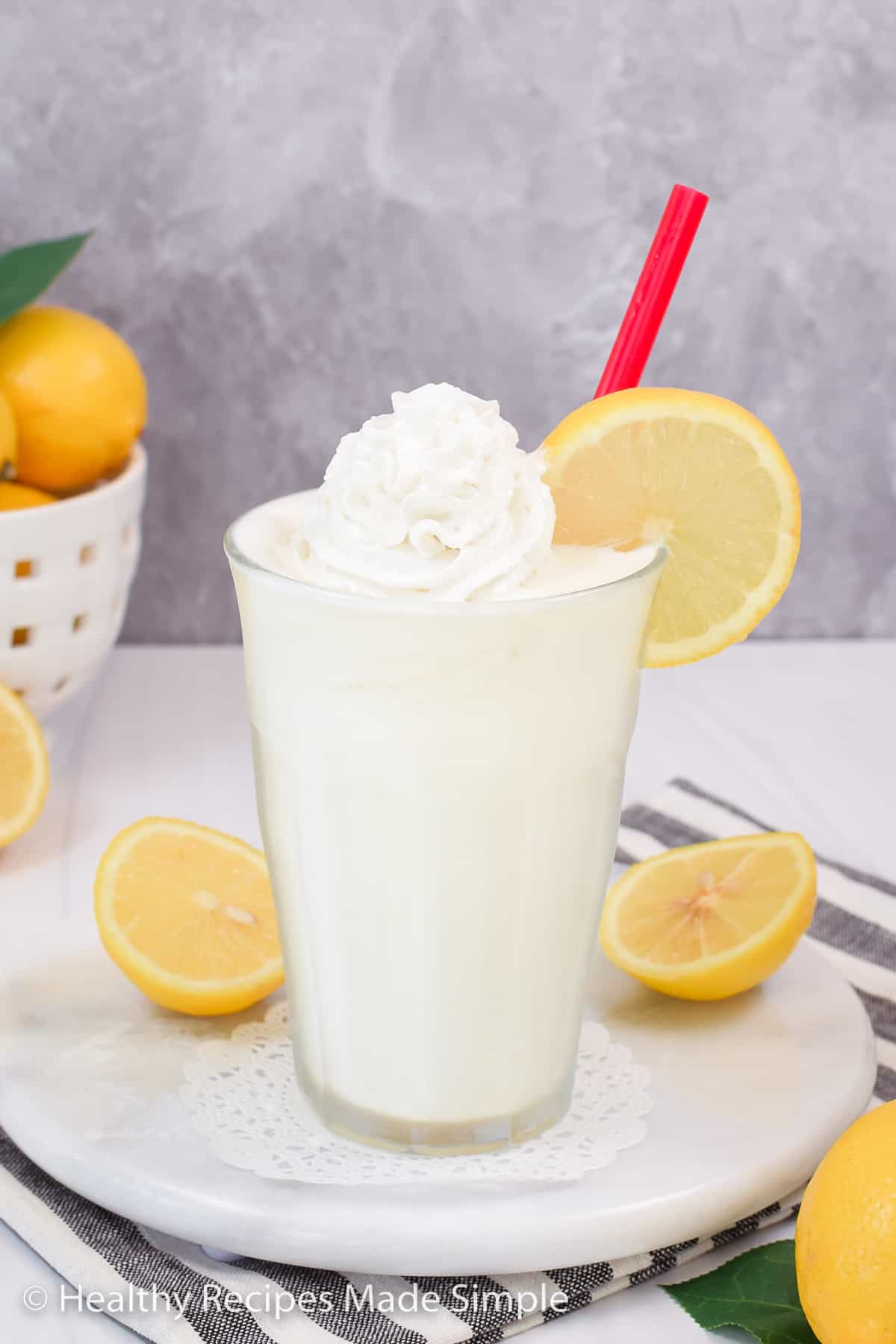 Lemon shake in a clear glass with lemons in the background.