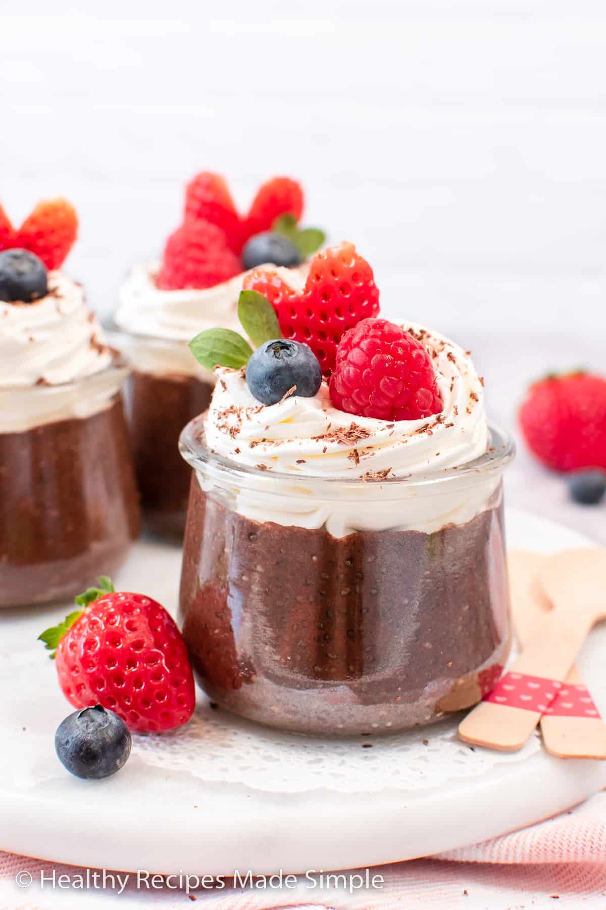 A clear jar of chocolate chia pudding topped with white cream and a heart shaped strawberry.