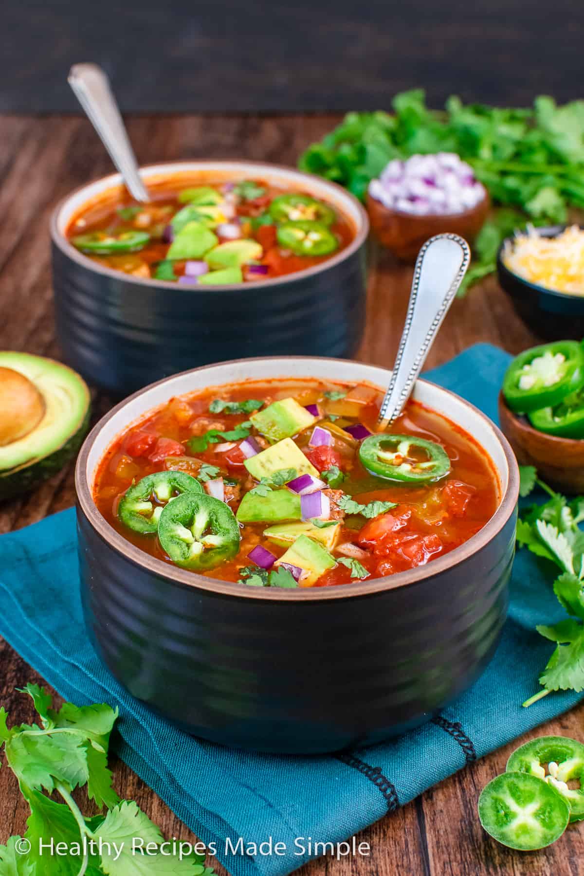 A bowl of chili without beans in a black bowl topped with jalapeño slices.