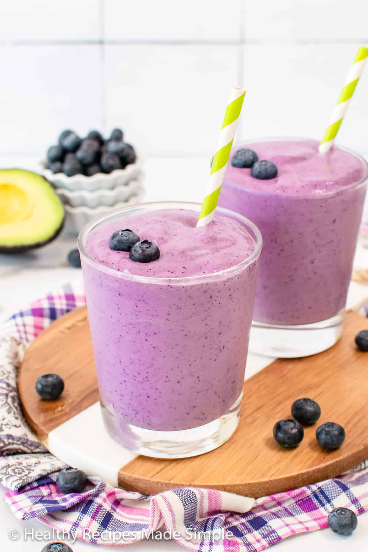 Blueberry avocado smoothie in a clear glass with a green and white straw.