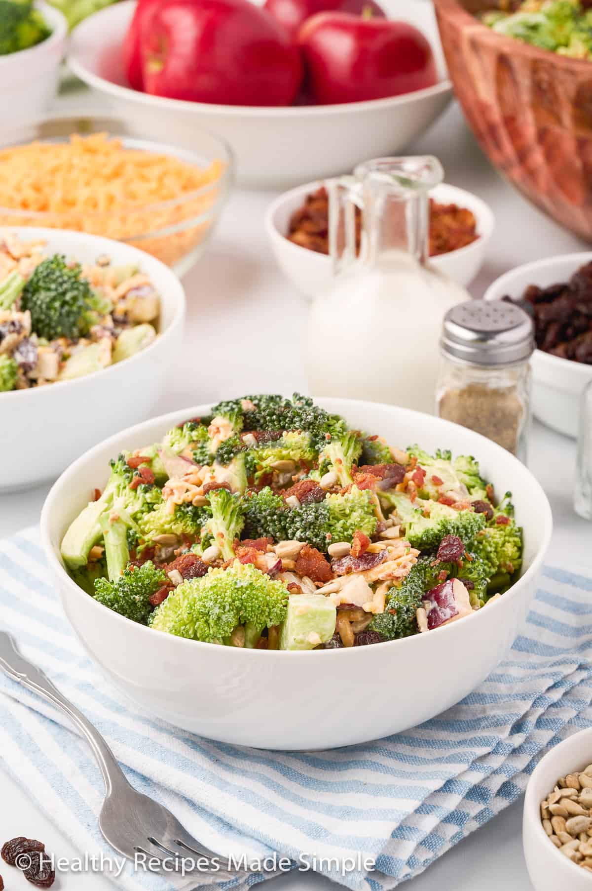 A white bowl filled with broccoli crunch salad with toppings in the background.