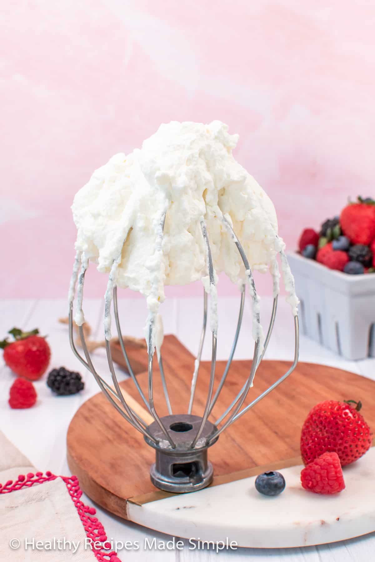 No sugar whipped cream on a whisk with berries in the background.