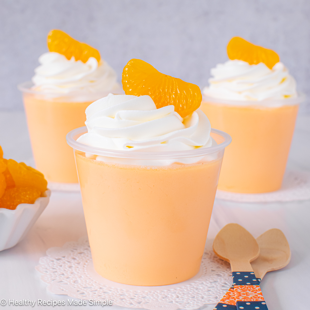 Three clear cups filled with orange protein Jello and topped with whipped cream.