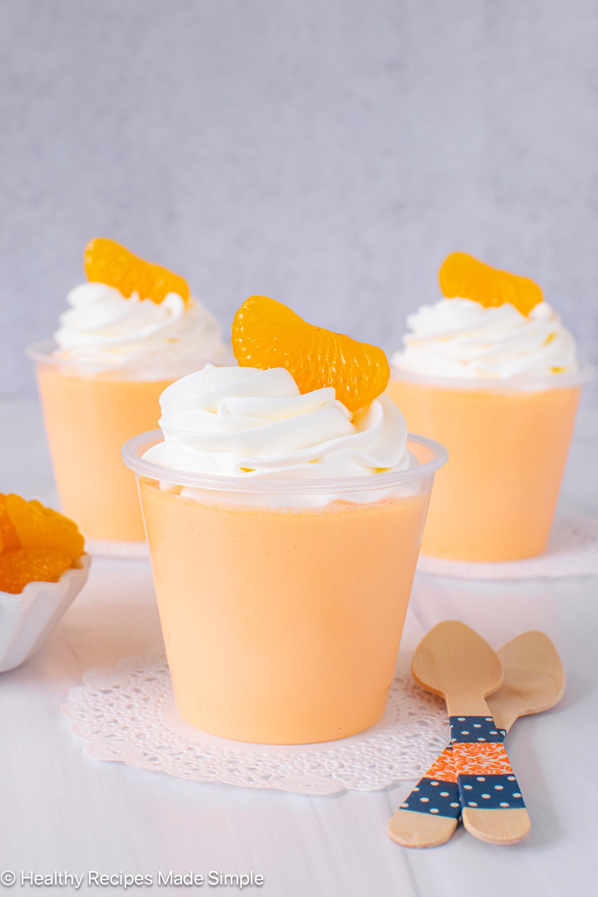 Three clear cups filled with orange protein Jello and topped with whipped cream.