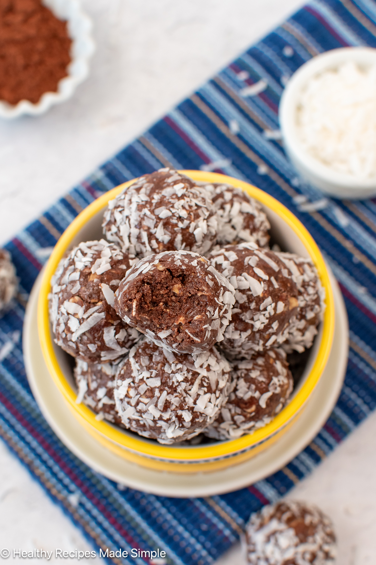 An overhead shot of a bowl of chocolate coconut balls with a bite out of one.