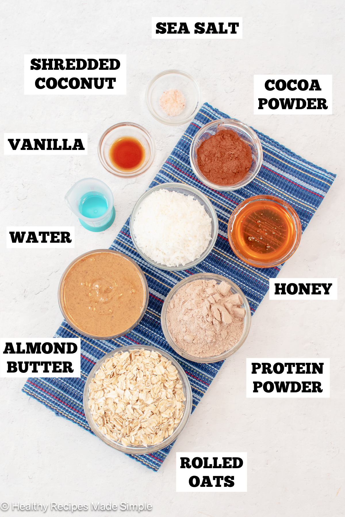 A white board with bowls of ingredients needed to make protein balls with coconut.